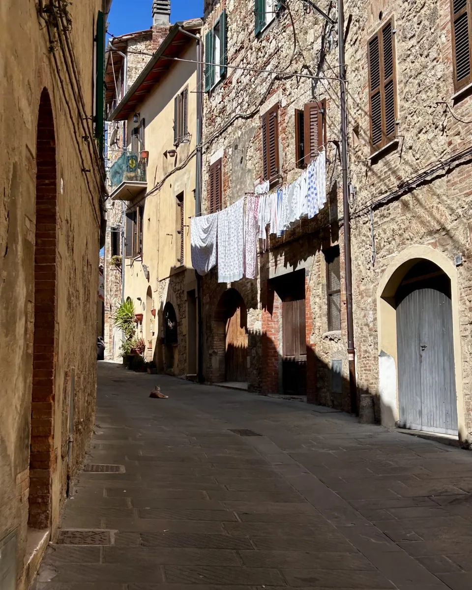 A quiet summer day in a small Italian town, with narrow cobblestone streets, rustic stone buildings, wooden shutters, an